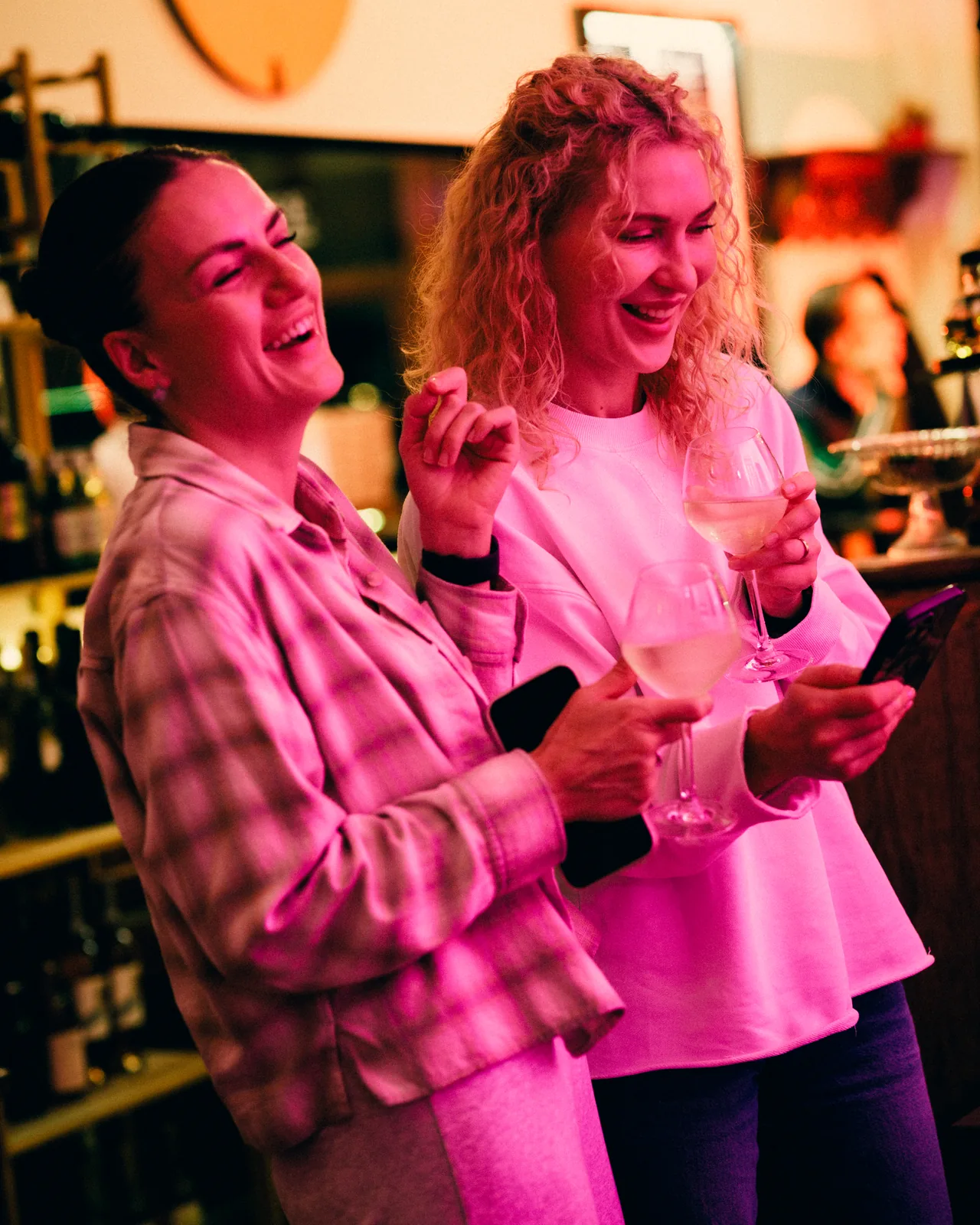 Deux amies rient au comptoir, un verre à la main